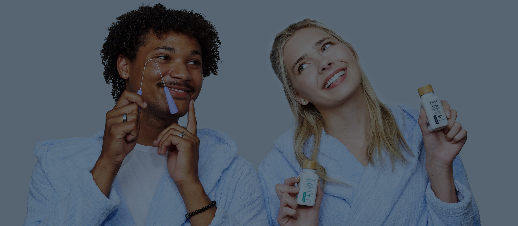 Two people in bathrobes, one using DrTung's Stainless Steel Tongue Cleaner and the other holding a bottle of HTT.