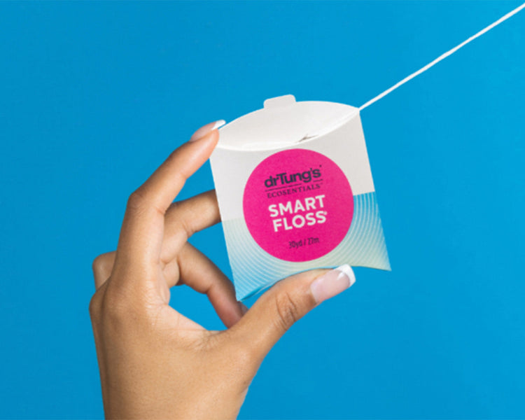 A hand holding a Smart Floss and pulling some floss over a blue background